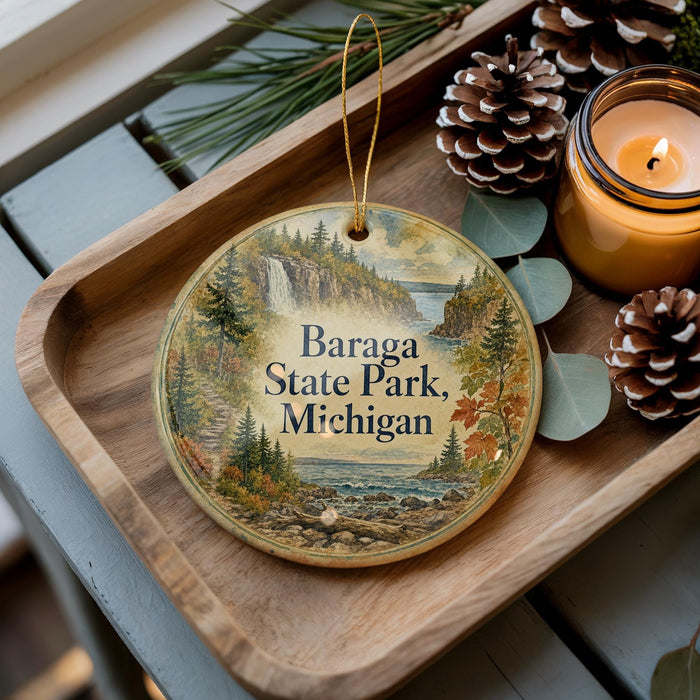 A decorative ornament with a scenic landscape of Baraga State Park, Michigan, featuring pine cones, a candle, and pine branches.