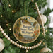 A circular ornament hanging on a Christmas tree, featuring a scenic landscape with a waterfall and pine trees.
