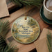 A round ornament with a scenic landscape of a lake, trees, and a lighthouse, hanging on a wooden surface.