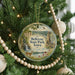 A round ornament hanging on a Christmas tree, featuring a scenic landscape with a waterfall, a castle, and a deer.