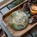 A decorative ornament featuring a serene scene of Big Lagoon State Park, Florida, with a bird, a turtle, and a boat in the water. The ornament is placed on a wooden tray, surrounded by pine cones and a lit candle, creating a cozy and festive atmosphere.