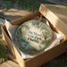 A decorative ornament in a brown box, featuring a scenic landscape with a bird and palm trees, with the text "Big Shoals State Park, Florida" printed on it.