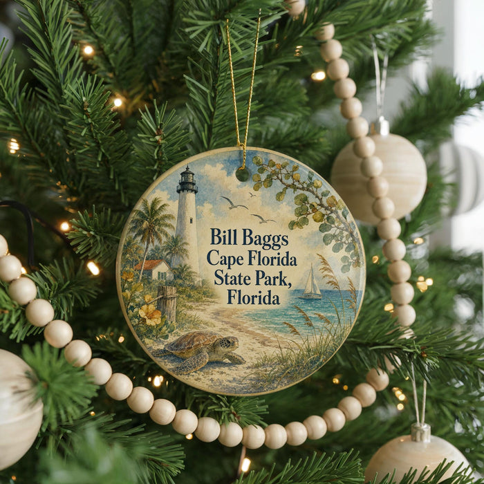 A round ornament hanging on a Christmas tree, featuring a lighthouse and palm trees, with the text "Bill Baggs Cape Florida State Park, Florida" printed on it.