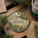 A decorative ornament featuring a scenic image of the Blackwater River State Park in Florida, surrounded by pine branches and flowers.