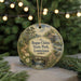 A round ornament with a painting of a scenic landscape, featuring a bridge, trees, and a river, hangs in front of a blurred background of Christmas lights.