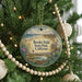 A round ornament hanging on a Christmas tree, featuring a scenic landscape with a beach, mountains, and wildlife.