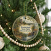 A round ornament hanging on a Christmas tree, featuring a scenic landscape with a castle, trees, and a river.