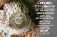 Ceramic ornaments, featuring a round ornament with a desert landscape and text, hanging in a basket with pine branches.