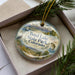 A decorative ornament in a box, featuring a scenic landscape with mountains, a lake, and various wildlife elements.