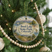 A round ornament hanging on a Christmas tree, featuring a scenic landscape with mountains, a lake, and a bird.