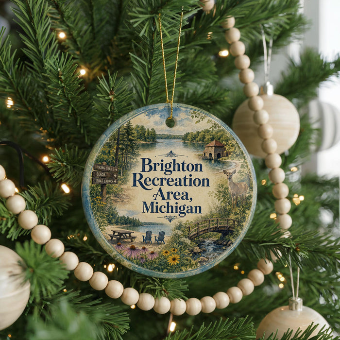 A round ornament hanging on a Christmas tree, featuring a scenic landscape with a lake, bridge, and trees.