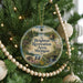 A round ornament hanging on a Christmas tree, featuring a scenic landscape with a lake, bridge, and trees.