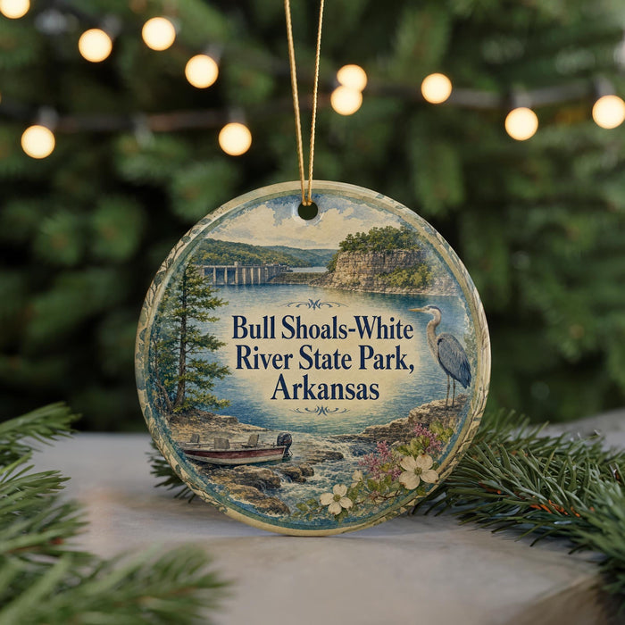 A round ornament with a scenic image of a river and a bird, surrounded by greenery, is displayed in front of a blurred background with twinkling lights.