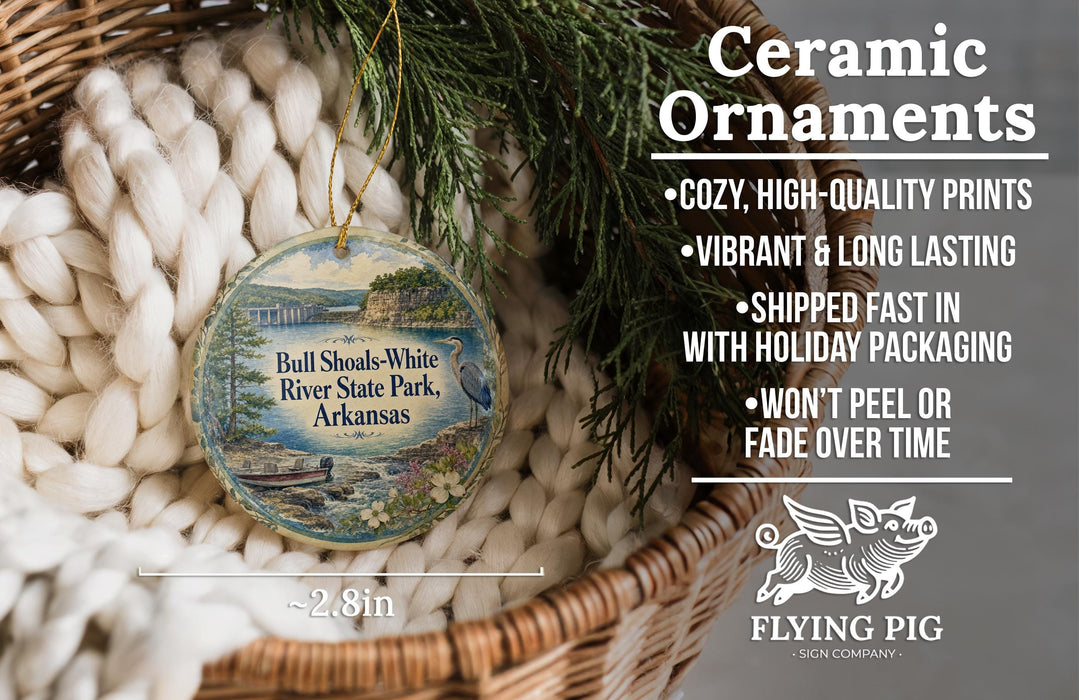 Ceramic ornaments, featuring a detailed image of the Ball Shakes-White River State Park in Arkansas, are displayed in a wicker basket. The ornaments are described as cozy, high-quality prints, vibrant, and long-lasting, and are shipped fast in holiday packaging. They are not to be peeled or faded over time. The image also includes a scale for size comparison and the logo of the Flying Pig Sign Company.