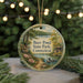 A round ornament with a scenic image of a lake and forest, featuring a bird and a cabin, hangs in front of a blurred background with twinkling lights.