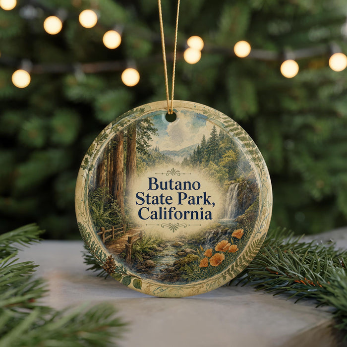 A circular ornament with a painting of a forest scene hangs in front of a Christmas tree with twinkling lights.