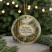 A circular ornament with a painting of a forest scene hangs in front of a Christmas tree with twinkling lights.
