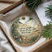 A decorative ornament with a natural scene, including a bird, a fish, and a seashell, is displayed in a box with pine branches.