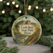 A decorative ornament featuring a scenic landscape with a castle, trees, and a river, hanging from a string.