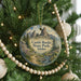 A round ornament hanging on a Christmas tree, featuring a scenic landscape with mountains and a winding path.