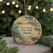 A round ornament with a beach scene and various wildlife, including a bird, deer, and turtle, is displayed against a blurred background of a Christmas tree with lights.