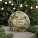 A round ornament with a painting of a house, palm trees, and a bird, along with the text "Cedar Key Museum State Park, Florida" on it, is displayed on a table with pine branches in the background.