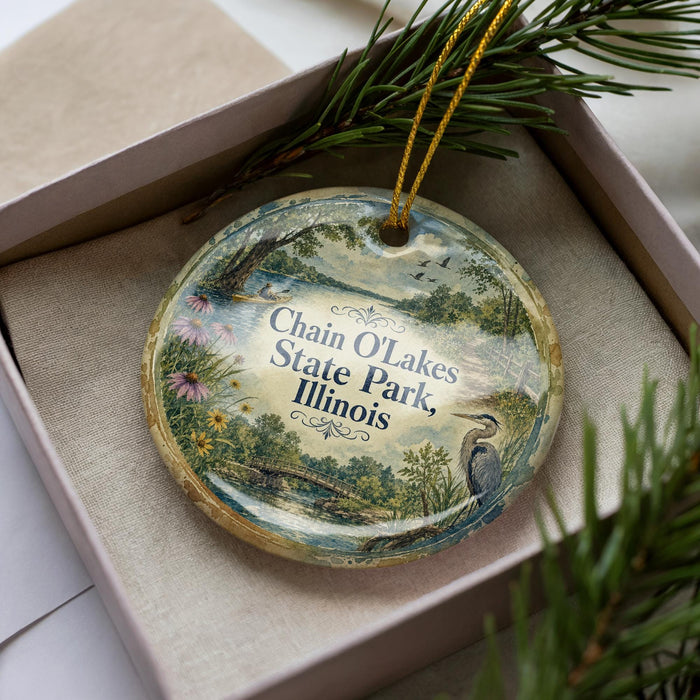 A decorative ornament in a box, featuring a scenic landscape with a lake, trees, and birds.