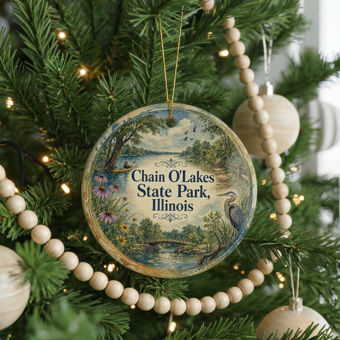 A round ornament hanging on a Christmas tree, featuring a scenic landscape with a lake and trees.