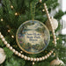 A round ornament hanging on a Christmas tree, featuring a scenic landscape with a lake and trees.