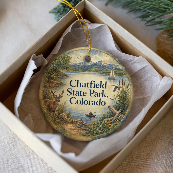 A decorative ornament in a box, featuring a scenic landscape with mountains, a lake, and various wildlife elements such as birds and deer.