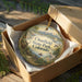 A decorative ornament in a box, featuring a scenic landscape with mountains, a lake, and various wildlife elements.