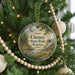 A round ornament hanging on a Christmas tree, featuring a scenic landscape with a lake and mountains.