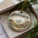 A decorative ornament in a box, featuring a scenic landscape with mountains and a wagon, representing the City of Rocks National Reserve in Idaho.