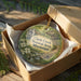 A decorative ornament in a cardboard box, featuring a scenic image of Clark Creek Natural Area in Mississippi.