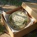 A decorative ornament in a box, featuring a scenic image of Clear Lake State Park, Michigan.