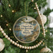 A round ornament hanging on a Christmas tree, featuring a scenic landscape with a lake, trees, and a boat.
