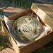 A decorative ornament in a box, featuring a scenic landscape with a waterfall and trees, with the text "Clinton State Park, Kansas" printed on it.