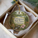 A decorative ornament in a box, featuring a scenic landscape with a forest, a river, and a deer.