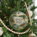 A circular ornament hanging on a Christmas tree, featuring a scenic image of Coldwater Lake State Park in Michigan.