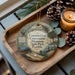 A decorative ornament featuring the Statue of Liberty and the Florida State Park, with the text "Constitution Convention Museum State Park, Florida" displayed on it. The ornament is placed on a wooden tray, with pine cones and a lit candle nearby.