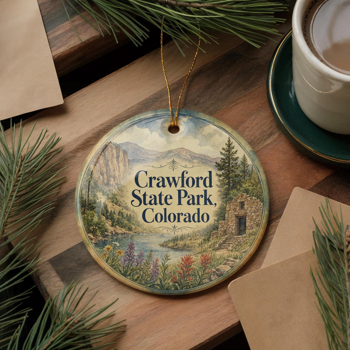 A decorative ornament featuring a scenic landscape of Crawford State Park, Colorado, with a mountain backdrop, river, and colorful wildflowers.