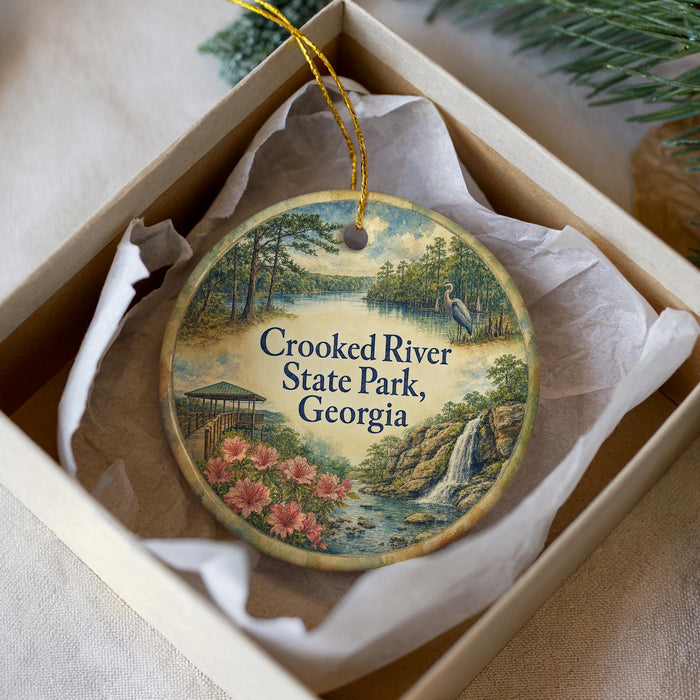 A decorative ornament in a box, featuring a scenic landscape with a river, waterfall, and flowers.