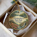 A decorative ornament in a box, featuring a scenic landscape with a river, waterfall, and flowers.