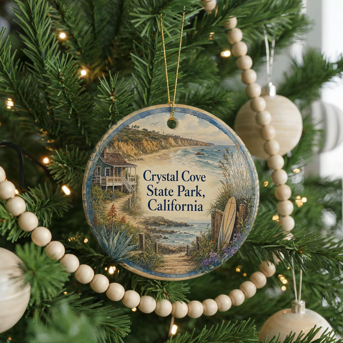 A round ornament hanging on a Christmas tree, featuring a scenic image of Crystal Cove State Park, California.