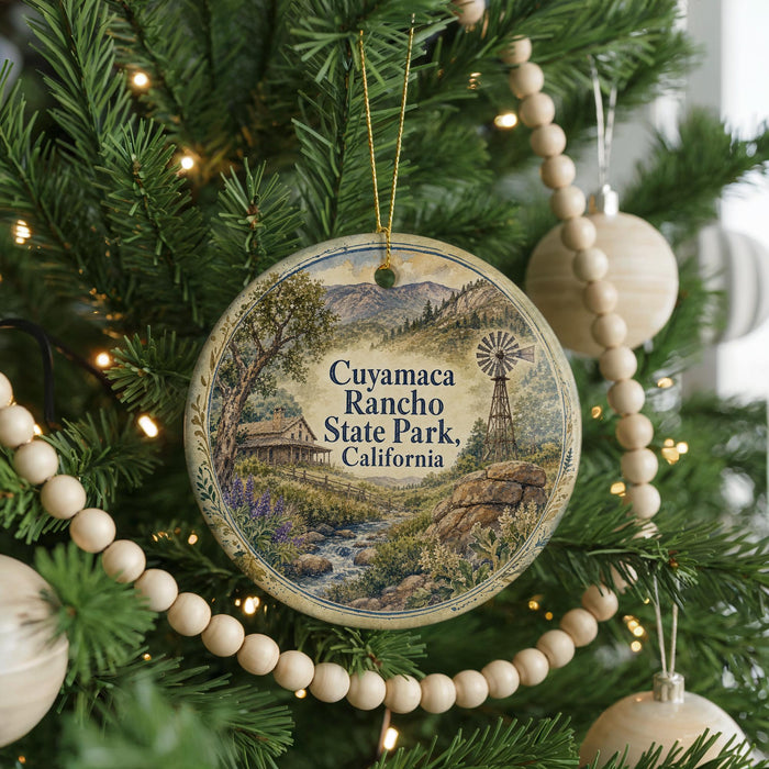 A round ornament on a Christmas tree, featuring a scenic landscape with a windmill and a river, surrounded by greenery and twinkling lights.