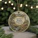 A round ornament with a scenic landscape of a river, mountains, and a windmill, hanging on a string.
