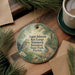 A decorative ornament with a bird and tropical plants, placed on a wooden surface next to a cup of coffee and some papers.