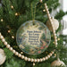 A round ornament with a bird and tropical plants is hanging on a Christmas tree, surrounded by beaded ornaments and twinkling lights.