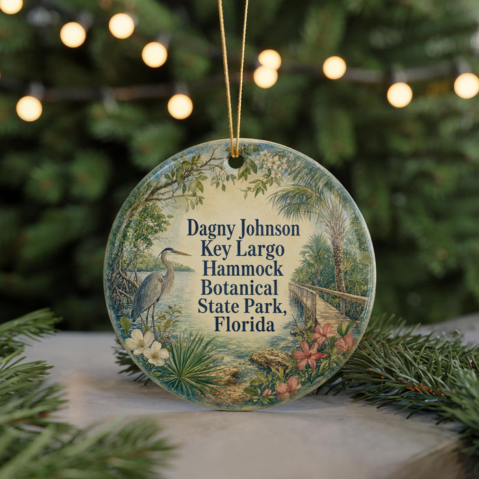 A round ornament with a tropical scene featuring a heron, palm trees, and flowers, hanging from a string.