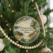 A Christmas tree decorated with ornaments, including a circular ornament with a scenic lake and forest landscape, and a beaded ornament.